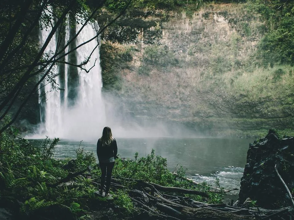A contemplative figure standing at a waterfall in nature